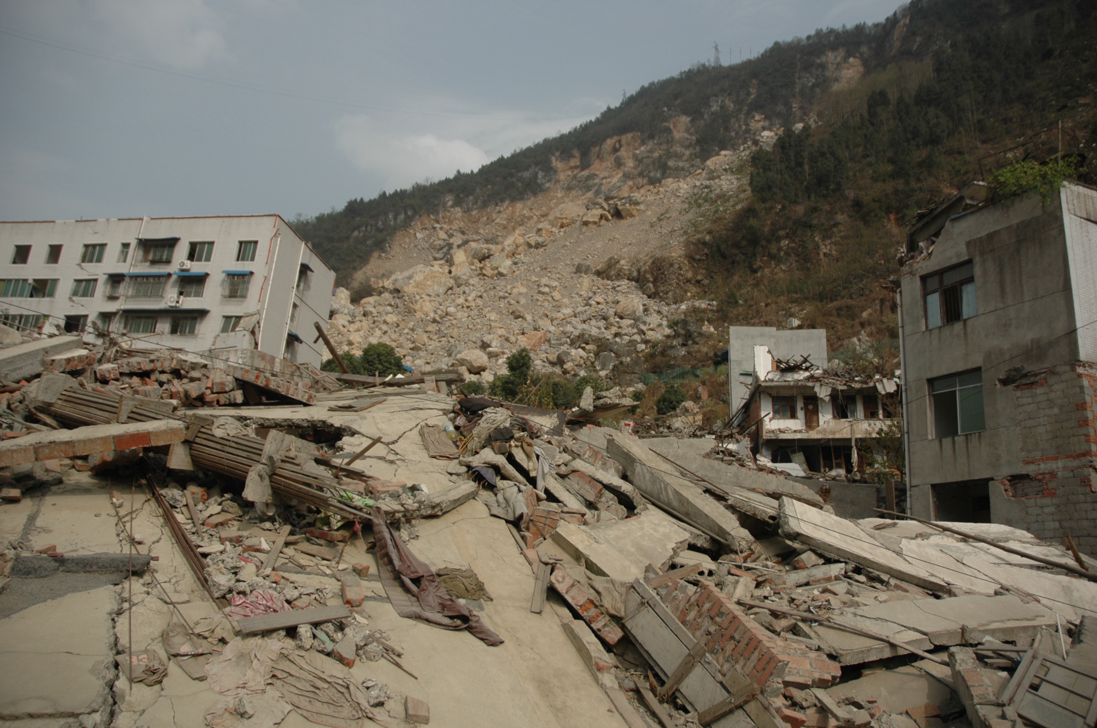 完全坍塌的房屋,远处是塌方过后的山体滑坡,当时这些滚滚落石不知道